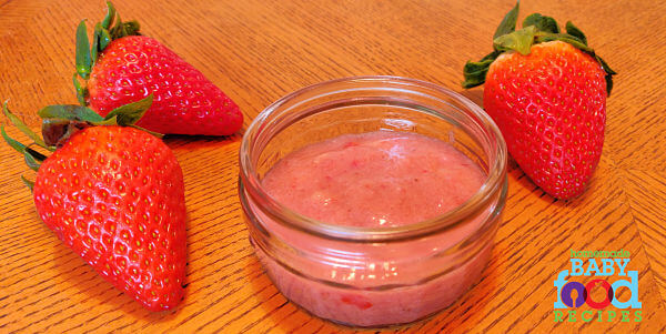 A bowl of strawberry and banana baby food puree, next to fresh strawberries