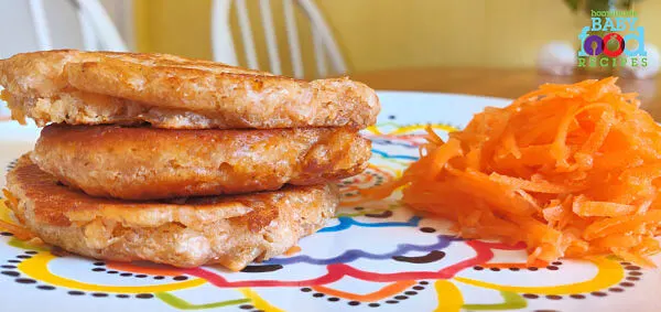 Three Carrot and Coconut Pancakes along with some grated carrot. Your baby will love these tasty, egg-free pancakes